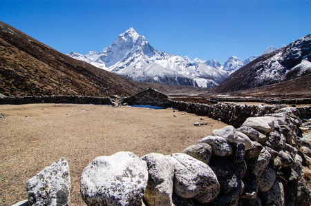 Stone barn with boundary is in front of the scenic view of high snow mountains on the Everest base camp trekking route in blue sky.の写真素材
