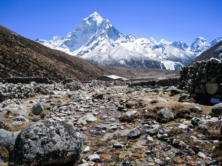 A stream runs through a village in himalayas with a view of high snow mountains in background on a blue sky day.の写真素材