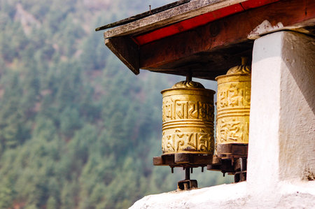 The sunshine is on the brass prayer wheels under the wooden roof in a village on the Everest base...