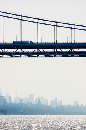 A double-decked suspension bridge, George Washington Bridge, over the Hudson river connects New Jersey and New York with silhouette of city skyline  behind.の写真素材