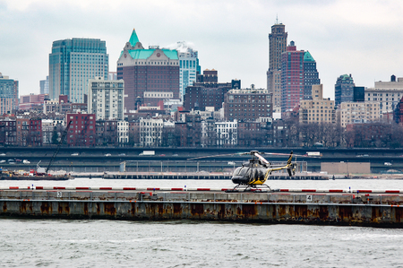 New York, USA - April 7, 2011: Yellow, black helicopter parked on the helipad, which is part of the pier on the East River of New York City against a backdrop of a skyscraper neighborhood of Brooklyn in the haze.のeditorial素材