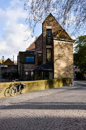 Bruges, Belgium - April 15, 2010: The evening sunlight shine to a bicycle leaning on a moss short fence of an old brick house on a cobblestone street in Bruges.のeditorial素材