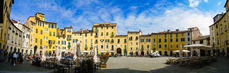Lucca, Italy - April 11, 2013: Panorama of Piazza Anfiteatro in Lucca, was ancient Roman amphitheatre, surrounded by old yellow buildings and outdoor restaurants with many tourists relaxing in blue sky on a sunny day.のeditorial素材