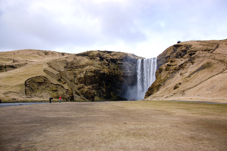 Iceland-April 7, 2016: A romantic couple taking photo in front of the SkÃÂ³gafoss, the waterfall in south Iceland, with the rocky cliff behind in bright sky on horizontal view.のeditorial素材