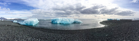 Panorama of blue ice floating near gravel beach, volcanic beach, from Atlantic Ocean with...