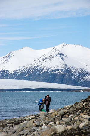 Iceland-April 9, 2016: Family tourists enjoyed the view on the gravel shore of the Jokulsarlon Glacier Lagoon with snow-capped mountain backdrop on bright blue sky at southeast Iceland in vertical view.のeditorial素材
