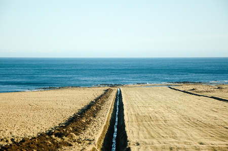 The natural drainage to the turquoise sea through the dry land around The eastern Fjords of Iceland in sunshine on clear blue sky.の写真素材