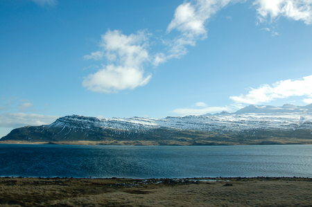Scenery of the road trip to the eastern fjords of Iceland with turquoise sea and snow mountain in sunshine on a blue sky day.の写真素材