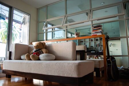 Teddy bear sitting on the sofa with cushions in the decorated living room of the middle-class condominium located in the heart of Bangkok.の写真素材