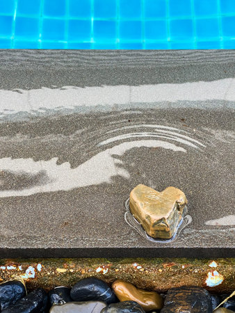 Brown heart-shaped pebbles sit on a dark gray tiled floor at the edge of a bright blue swimming pool...