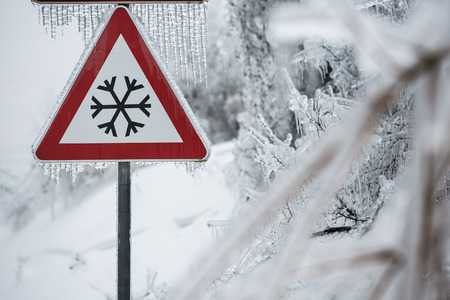 Traffic sign for icy road with sleet covered treesの写真素材