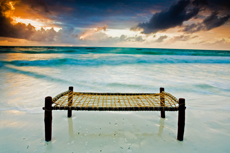 Bed on a sandy beach touching the sea under dramatic skyの写真素材