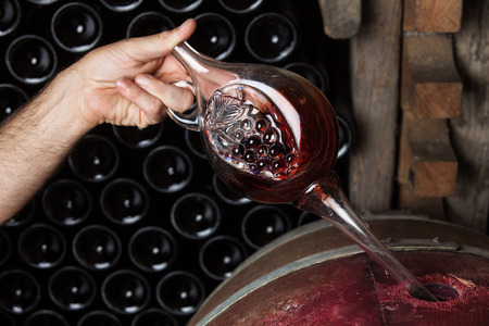 Sommelier sampling red wine from oak barrel, bottles in the backgroundの写真素材