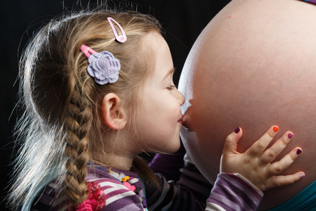 Adorable little girl kissing the belly of a highly pregnant mother, in expectation of a siblingの写真素材