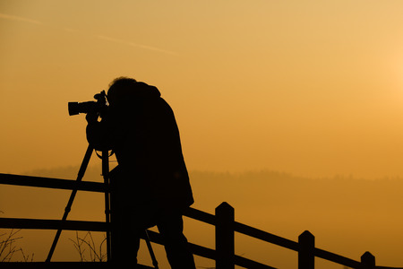 Silhouette of a photographer taking photos of an amazing sun at the top of a hillの写真素材