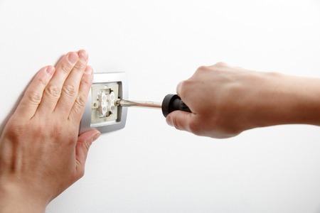 Electrician installing a silver light switch with a screwdriver on a white wall, renovating home.の写真素材