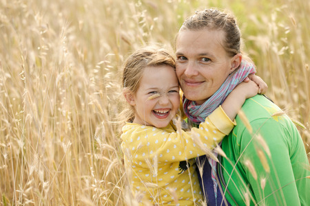 Caucasian mother and daughter hugging, smiling and sharing a tender bonding moment amongst meadow grass. Mothers day concept. Serenity and tranquility.の写真素材