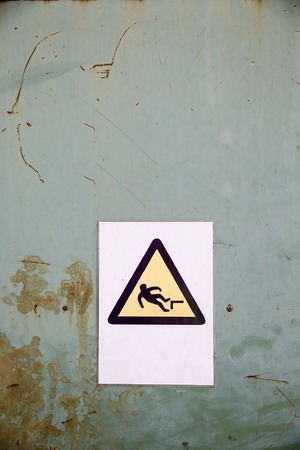 Actual fall (trip) hazard sign, symbol warning workers and passers-by of danger and risk of falling, on uniform industrial rusty steel background. Safety and liability measures concept.の写真素材