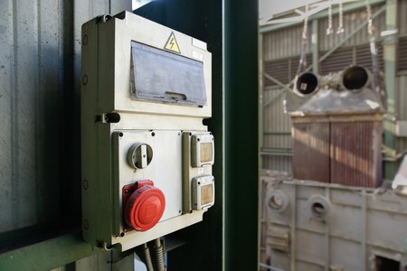 Weathered industrial electricity cabin, electrical junction box  with red shut off (stop) button for emergencies. Industrial setting in the background.の写真素材
