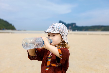 Child on a trip to a sandy tropical beach in summer, drinking bottled water with soluble electrolytes for rehydration.の写真素材