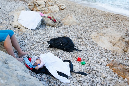 Sleeping baby with a pacifier lying on a pebbled beach in improvised bed during a family vacation. Family on vacation, adaptable baby and relaxed parenting concept.の写真素材