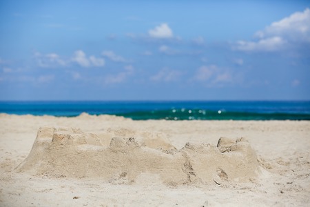 Sand castle on a sandy beach, lit by bright sunlight with cloudscape and deep blue sea in the background. Summer activities and vacation concept.の写真素材