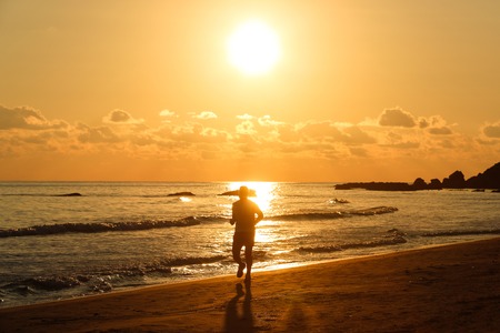 Silhouette of a fit runner at sunset on a sandy beach, enjoying the evening chill of late summer. Active lifestyle, vacation recreation, outdoor activity concept.の写真素材