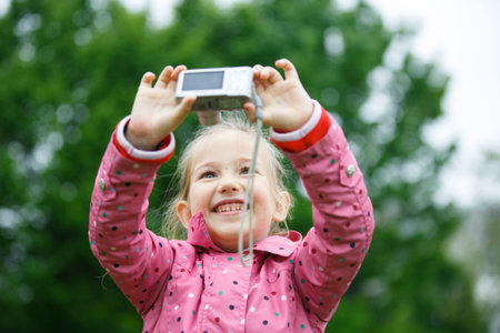 Little cheerful girl making a selfie with digital camera, enjoying her time on a dandelion meadow. Active lifestyle, curiosity, pursuing a hobby, technology and kids  concept.の写真素材
