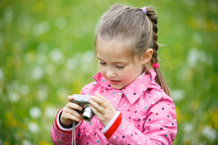 Little girl checking and reviewing photos she made with digital camera, enjoying her time on a dandelion meadow. Active lifestyle, curiosity, pursuing a hobby, technology and kids concept.の写真素材
