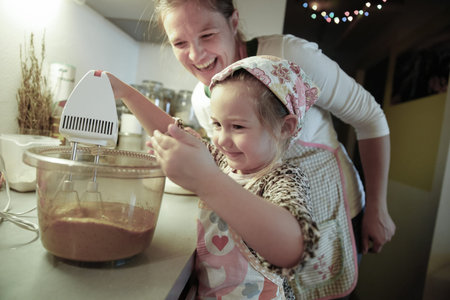 Mother smiling and tutoring her daughter in the kitchen as she is preparing dough for homemade...
