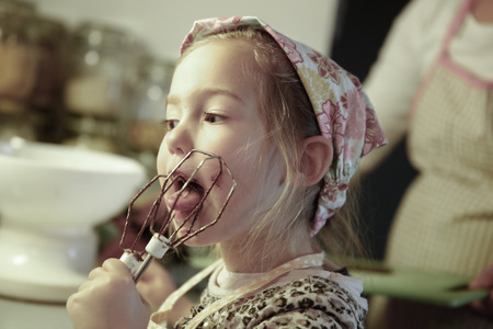 Little girl licking chocolate off the mixer beater after mixing dough for birthday cake. Permissive parenting, learning through experience, child inclusion, homemade food concept.の写真素材