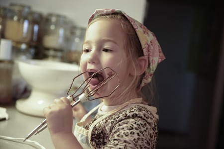 Little girl licking chocolate off the mixer beater after mixing dough for birthday cake. Permissive parenting, learning through experience, child inclusion, homemade food concept.の写真素材