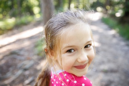 Little cheerful, big-eyed girl enjoying a hike through the woods, wandering and exploring nature. Active, outdoor lifestyle, family sports, quality time and happy childhood concept.の写真素材
