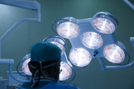 Silhouette of a surgeon during a real operation, illuminated by operating lights in the background. Medicine, technology, professional care concept.の写真素材