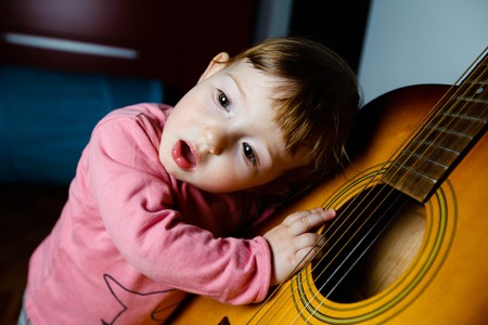Small toddler listening and singing to sounds, coming out of a guitar. Musical education, tactile experiences and learning concept.の写真素材