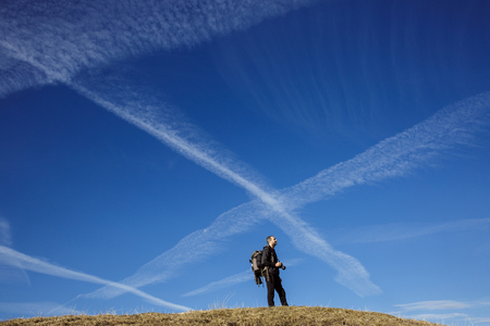 Hiker photographer on a mountain top admiring the surrounding alpine landscape, enjoying the view. Active lifestyle, natural environment, freedom and sports concept. Big blue sky in the background.の写真素材