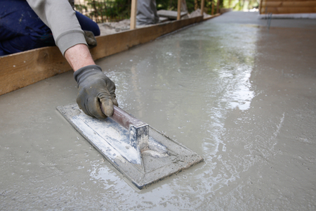 Mason leveling and screeding concrete floor base with square trowel in front of the house. Construction business, do-it-yourself, precision work around the house concept.の写真素材