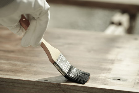 Carpenter holding a paintbrush over wooden surface, protecting wood for exterior influences and...