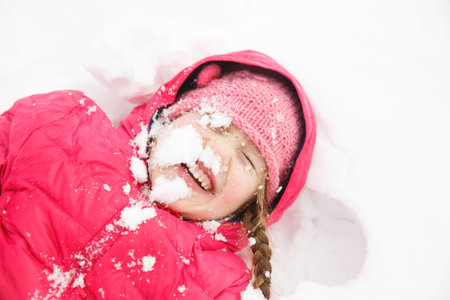 Playful girl with braids playing in snow, throwing it in the air, having fun and being active....