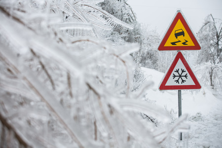 Dangerous and icy road sign with sleet covered trees. Danger on the road, black ice danger, wintertime concept. の写真素材
