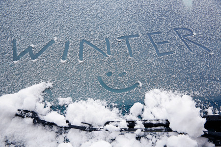 Word "winter" and a smiley drawn on snowy car windshield. Wintertime, fun, weather and cold concept. の写真素材