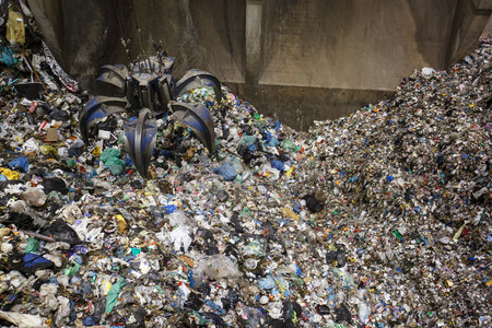 Mechanical claw hand grabbing pile of mixed waste, deposited in the waste treatment plant depot, preparing it for separation and treatment. Waste disposal, management, reuse, recycle and recovery concept. 
の写真素材