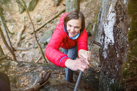 Woman climbing rock in the forest, holding security railing, ascending to the top, succeeding. Active lifestyle, progress and improvement, conquering challenges concept. の写真素材