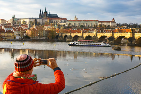 Tourist taking pictures of fall Prague cityscape with Charles Bridge across Vltava and the Hradcany castle complex. Travel, vacation, sightseeing concept with negative and copy space.のeditorial素材