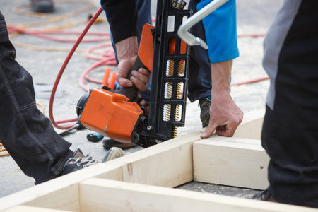 Professional carpenter using pneumatic nail gun on construction site. Occupational hazard,...