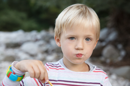 Boy eating in nature, having picnic with his family on the river bank. Outdoor lifestyle, positive parenting, childhood experience concept. の写真素材