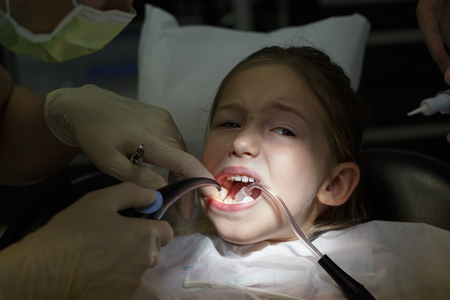 Scared little girl at the dentists office, in pain during a treatment. Pediatric dental care and fear of dentist concept. の写真素材