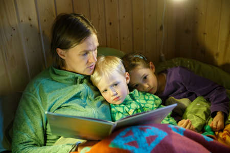 Mother reading bedtime stories to her children before going to sleep. Educational, motherhood, childhood, family concept.の写真素材