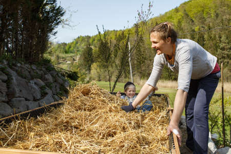 Son helping mother layering straw mulch in a raised garden bed. Quality time together. Sustainable living.の写真素材
