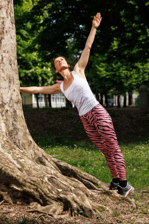 Woman working out before fitness training session in the park. Healthy young woman warming up outdoors.の写真素材